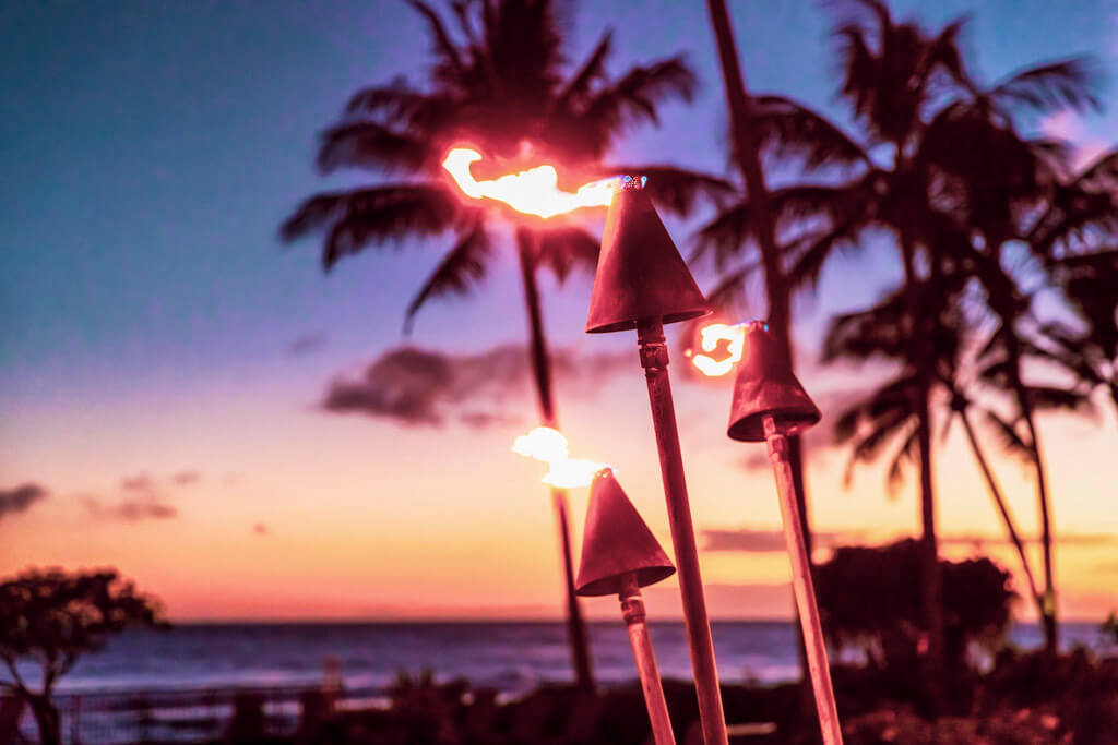 Flaming torches with palm trees in the background at sunset. our Oahu budget guide helps you see them for free.