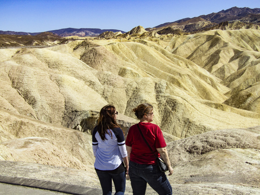 Two women overlooking the gold badlands peaks on a day trip to Death Valley.