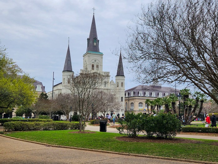 St. Louis Cathedral viewed across Jackson Square, from the west, with the open courtyard before the gray spired church. Visiting is one of the essential things to do in New Orleans.